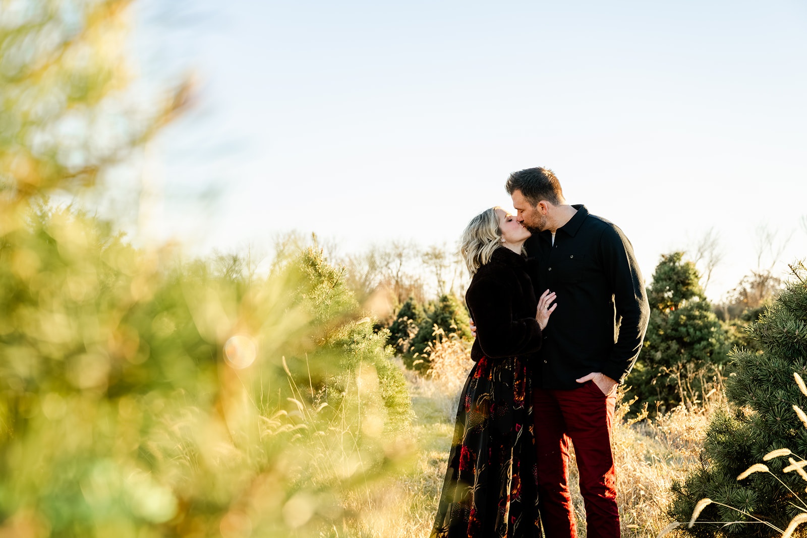 A happy couple in black and red kiss while standing among christmas trees