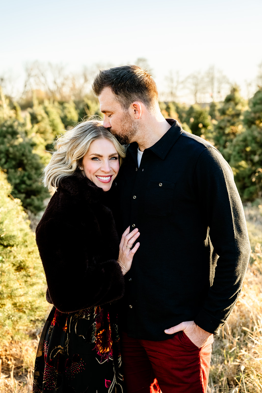 A smiling woman in a black sweater leans into the chest of her husband as he kisses her head at sunset before heading to romantic restaurants in Naperville