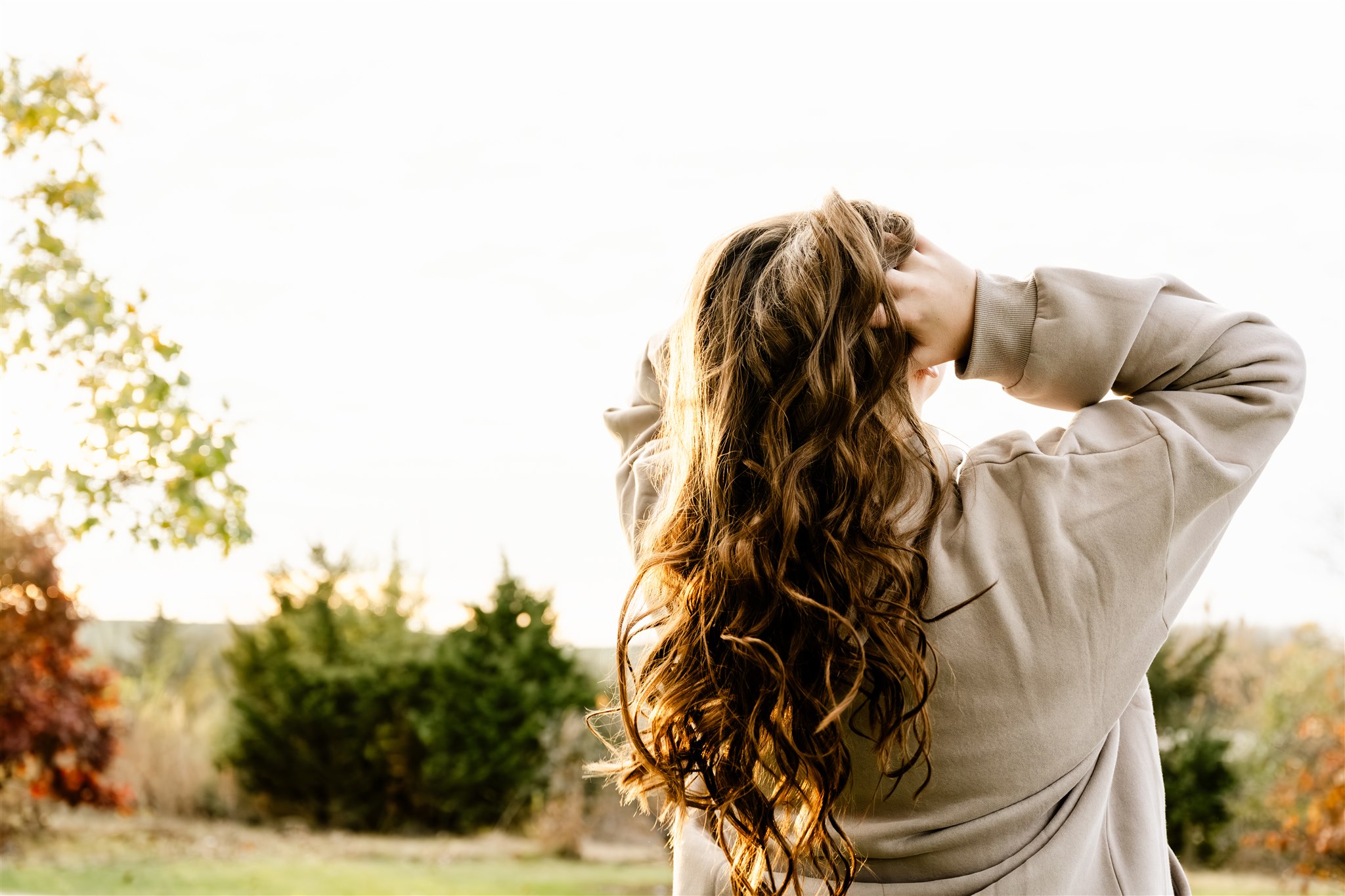 Details of a woman's brown hair in the sunlight as she fluffls it