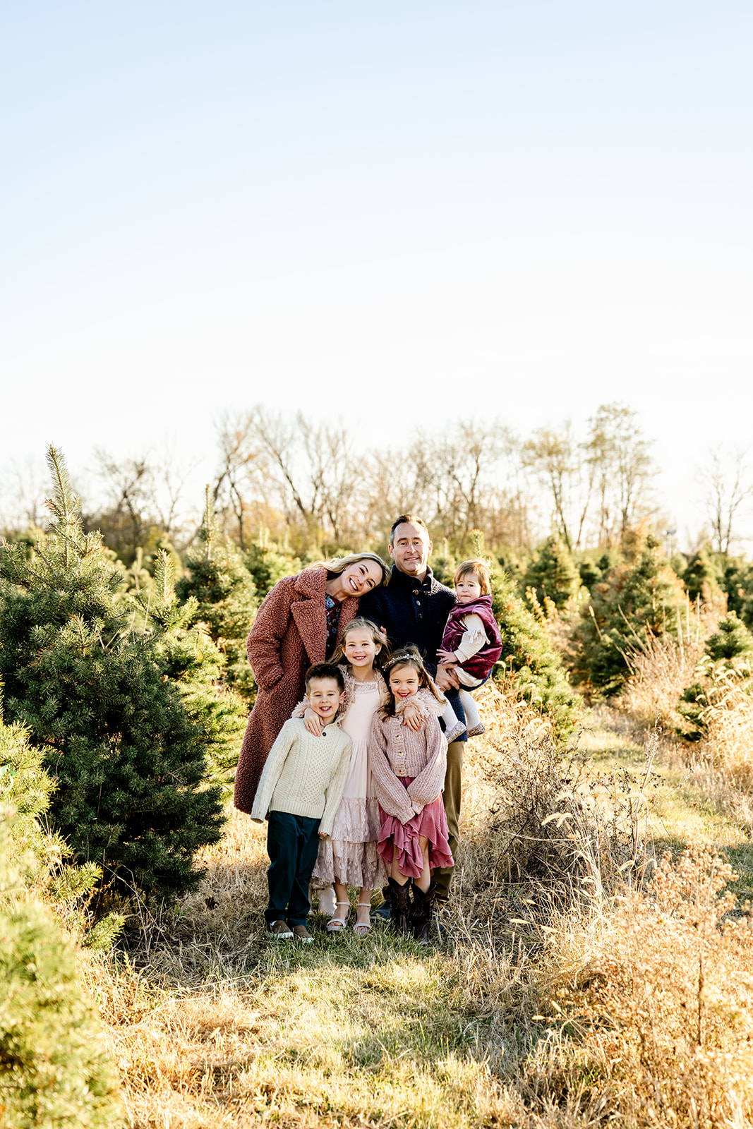 A happy family stands smiling together in a christmas tree farm