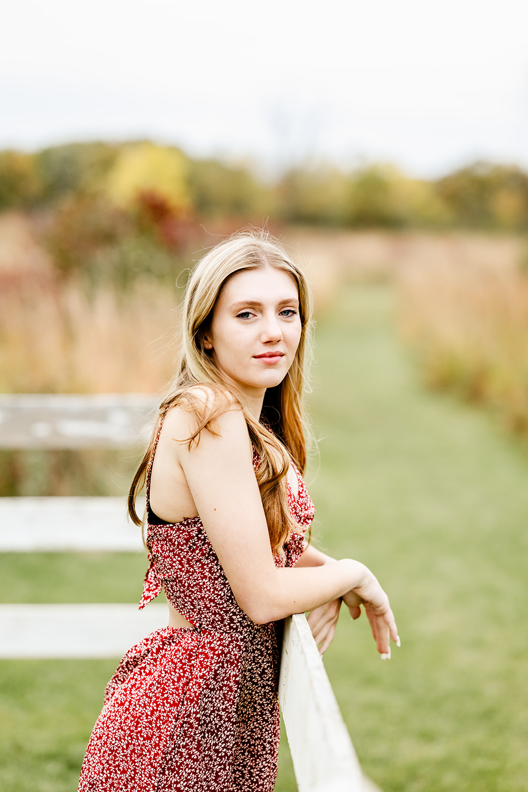 A high school senior in a red dress leans on a rustic wood farm fence at sunset after some SAT prep in North Shore Chicago
