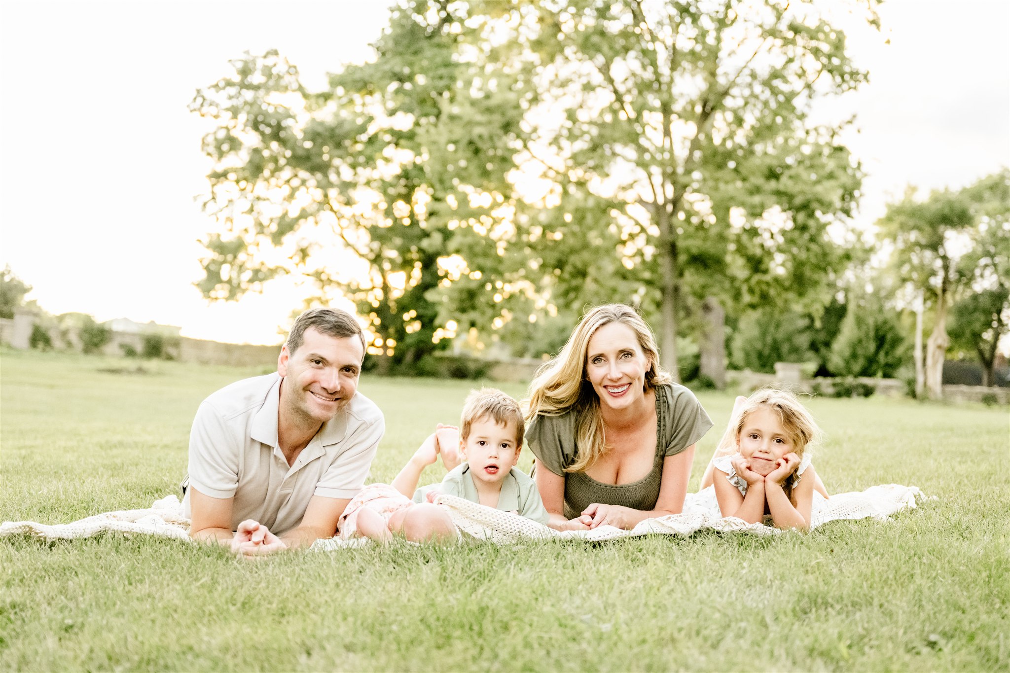 A mom and dad lay on a picnic blanket with their newborn and two toddlers before some swim lessons in North Shore