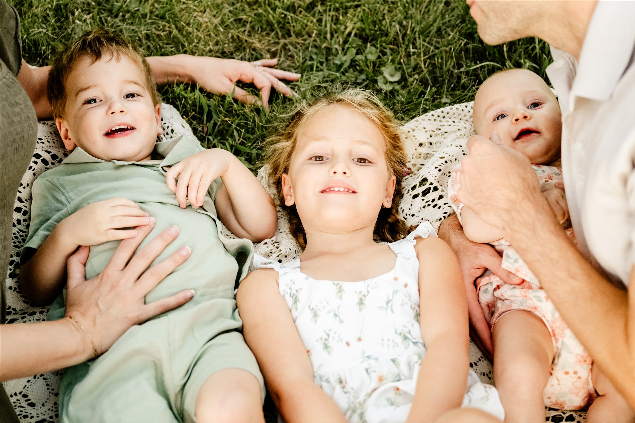 Toddler brother and sister lay on a picnic blanket while being tickled by mom and dad after some swim lessons in North Shore
