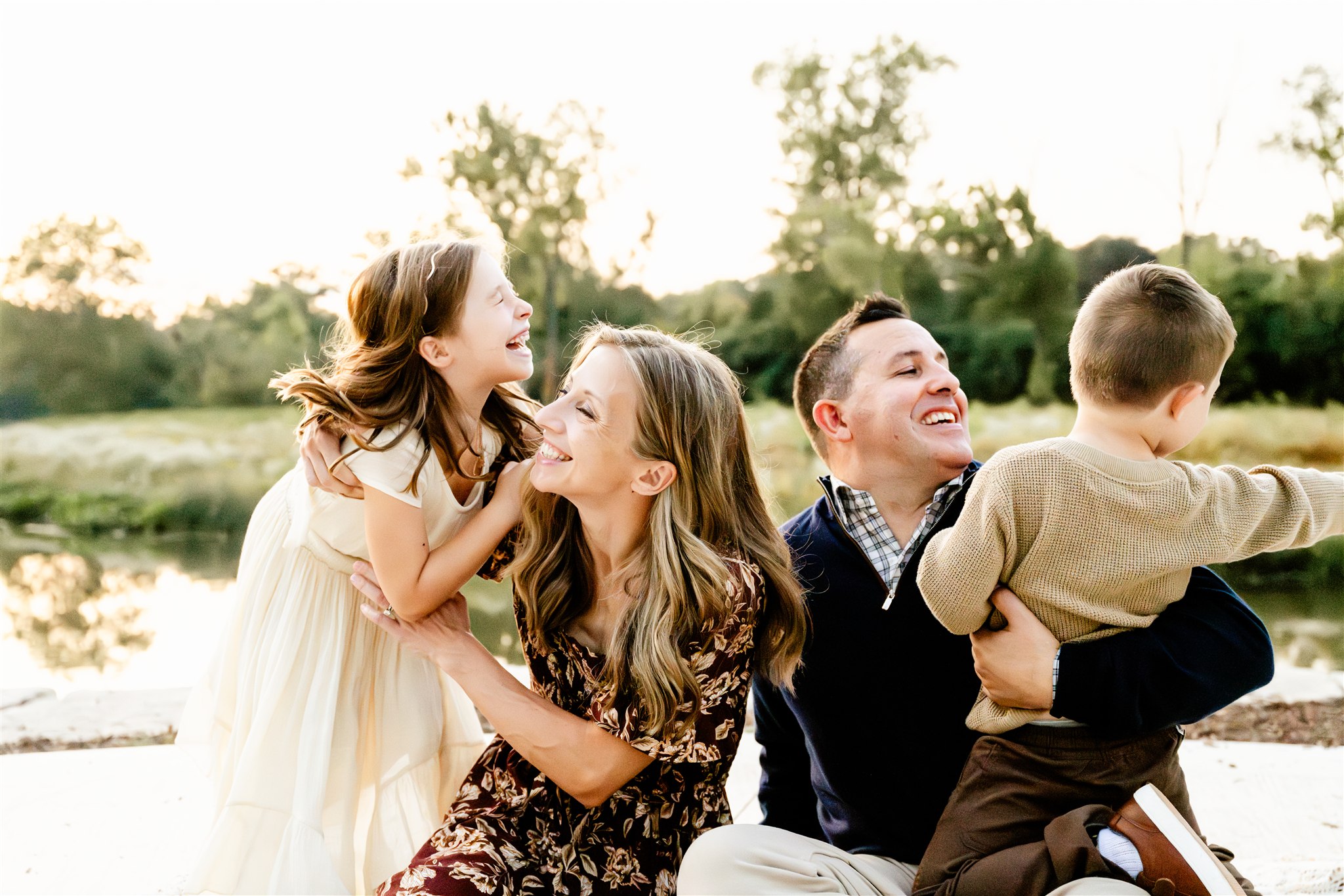 Laughing mom and dad play with their toddler son and daughter in their laps in a park