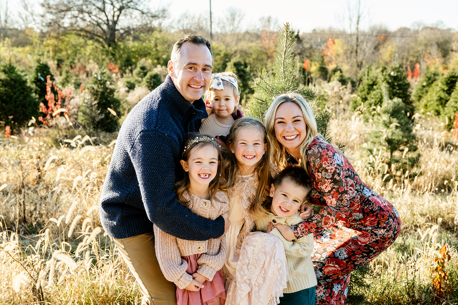 A happy family enjoys their time hugging their four children in a christmas tree farm