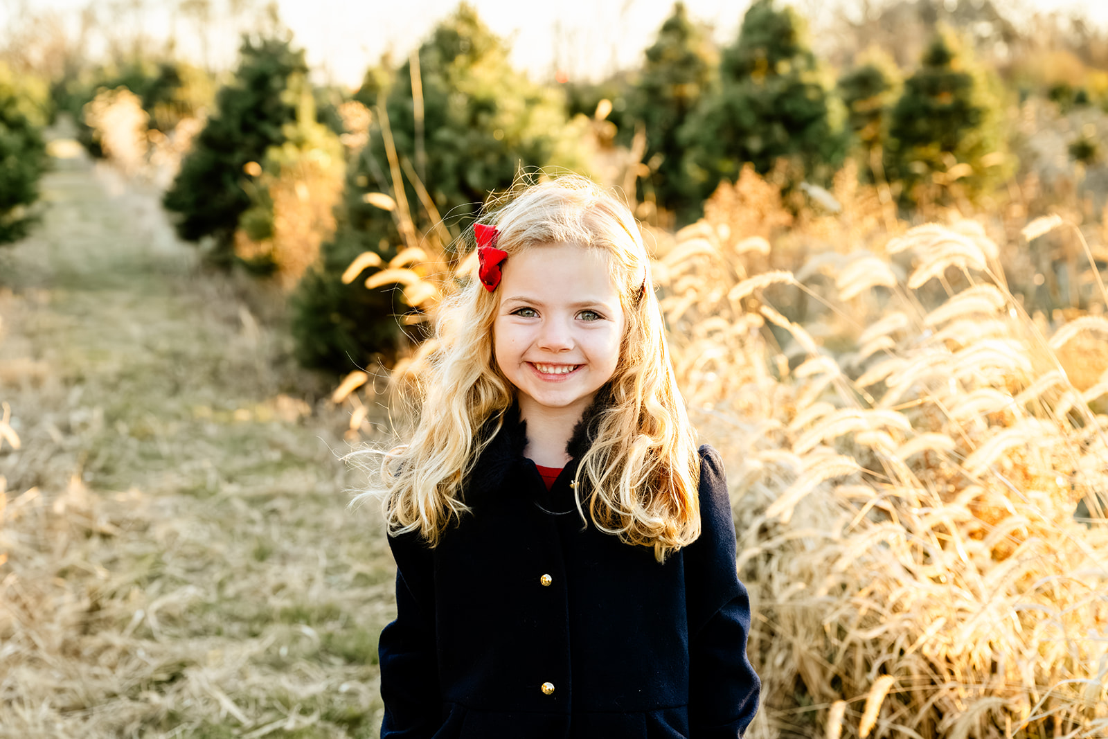 A smiling young blonde girl in a black coat in tall golden grass